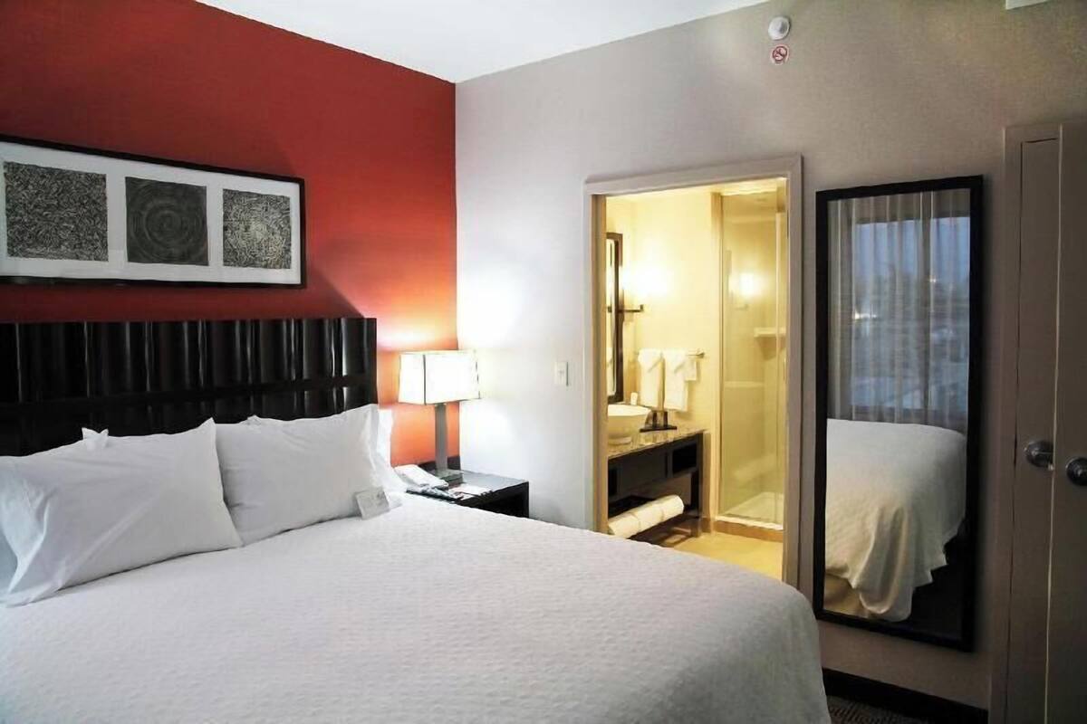 Une chambre d’hôtel comprenant un lit, une table de chevet, une lampe, un miroir et une porte donnant accès à une salle de bain.
