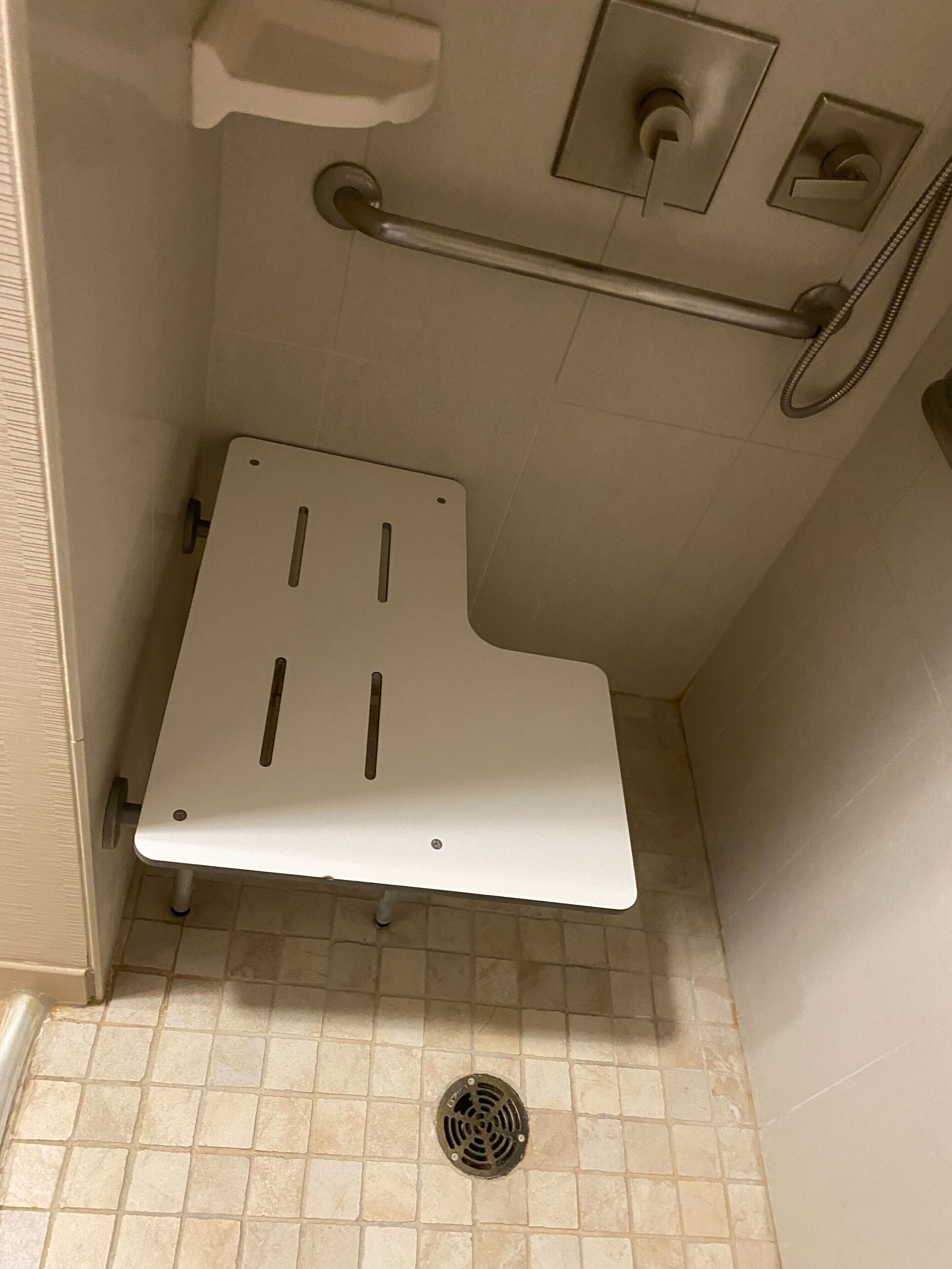 Een badkamer met een wit toilet, een handgreep, bedieningspaneel voor de douche en een betegelde vloer.