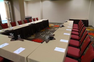 Un salón de conferencias con una larga mesa, sillas rojas y una alfombra con un diseño circular.