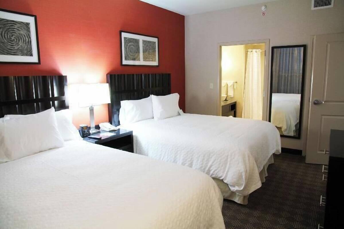 Une chambre d’hôtel avec deux lits, une table de chevet, une lampe, un miroir et une porte donnant sur une salle de bain.