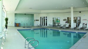 Ein Innenpool mit klarem Wasser, umgeben von Liegestühlen und einem gefliesten Boden.