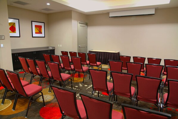 Un salón de conferencias con sillas rojas dispuestas en filas, una mesa y una chimenea.