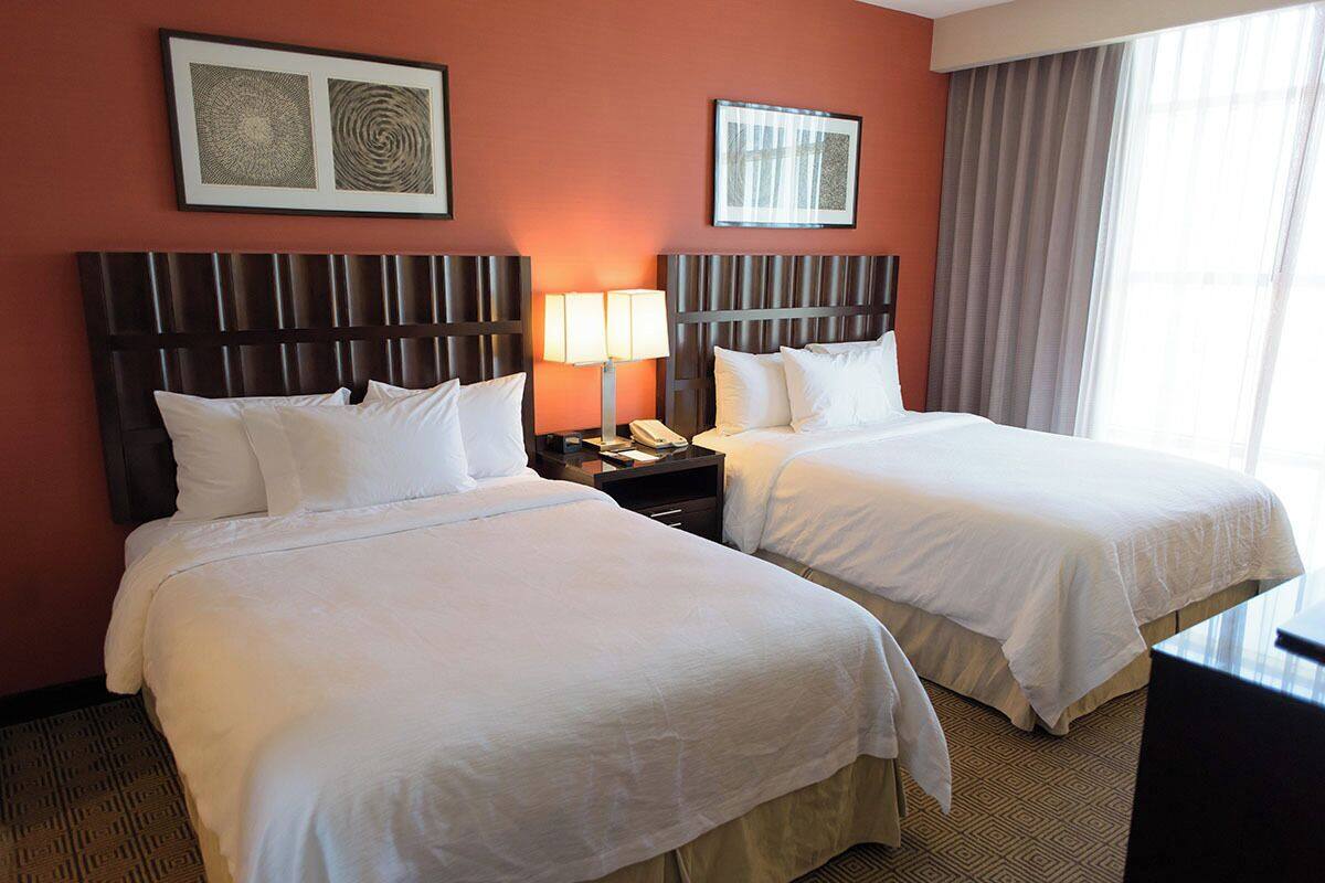 A hotel room with two beds, a nightstand with a lamp, and artwork on the walls.