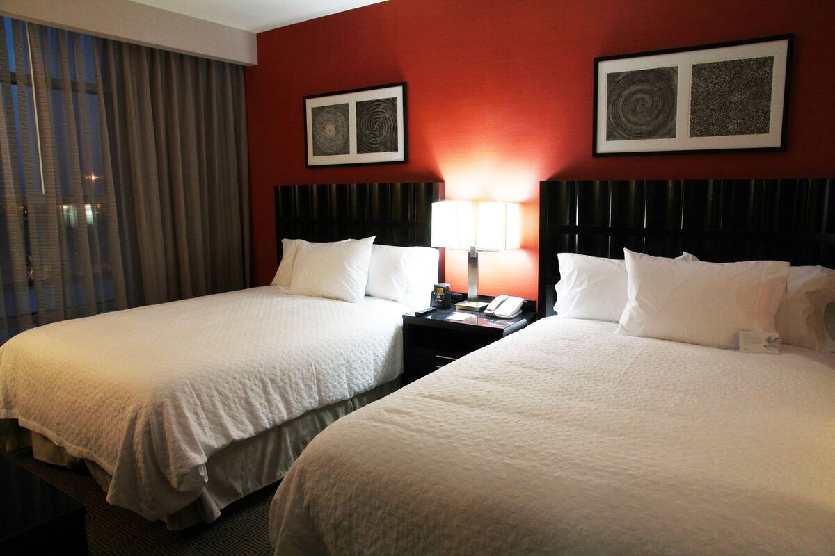 A hotel room with two beds, a nightstand with a lamp, and two framed pictures on the wall.