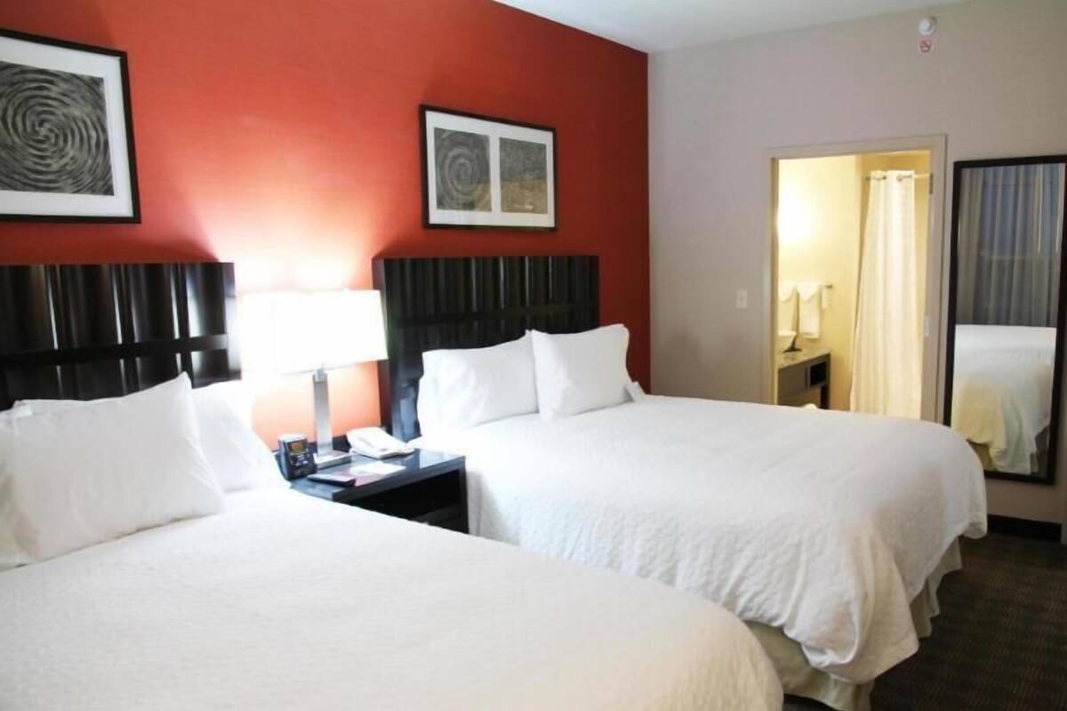 Une chambre d’hôtel avec deux lits, une table de chevet avec une lampe, un téléphone et un miroir.