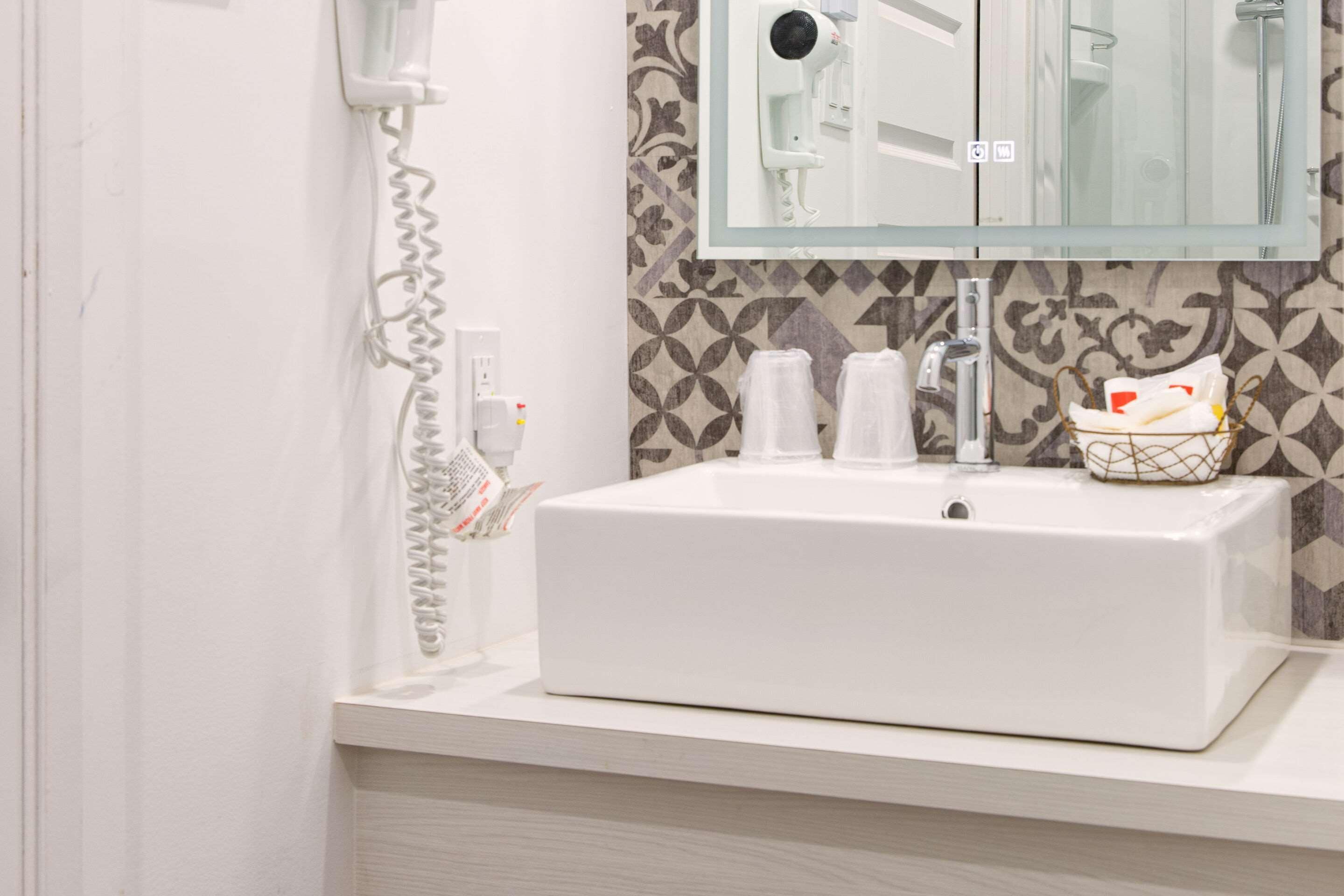 Ein Badezimmer mit einem weißen Waschbecken, einem Glasregal darüber und einer Wand mit Muster.