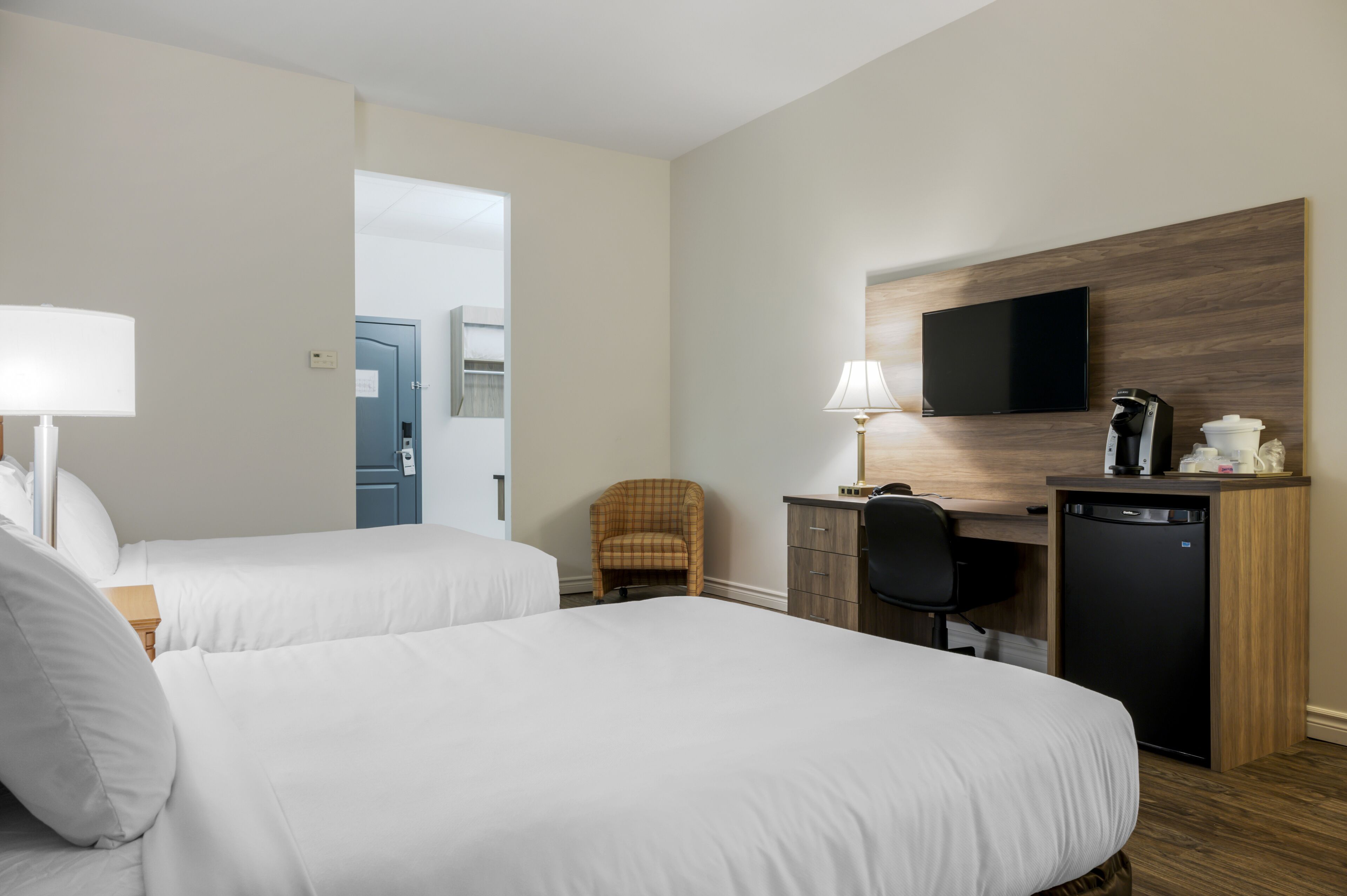 Quarto de hotel com duas camas, uma escrivaninha com cadeira, televisão e cafeteira.