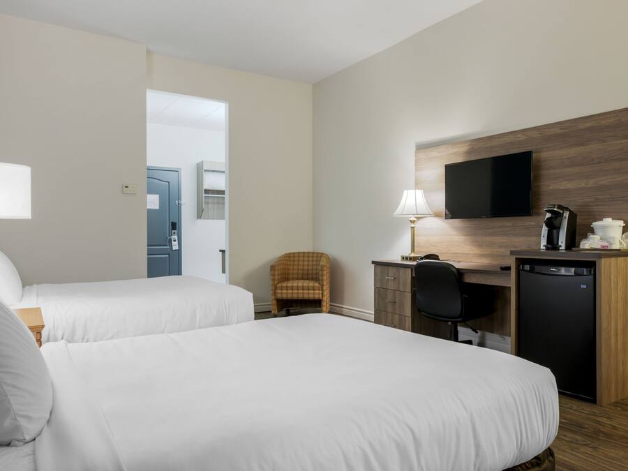 Quarto de hotel com duas camas, uma escrivaninha com cadeira, televisão e cafeteira.