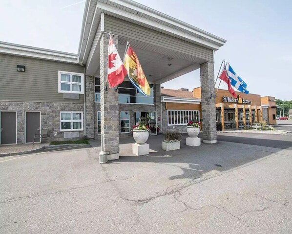 A hotel with a covered entrance, stone facade, and flags. - Econo Lodge Inn & Suites (Montmagny)