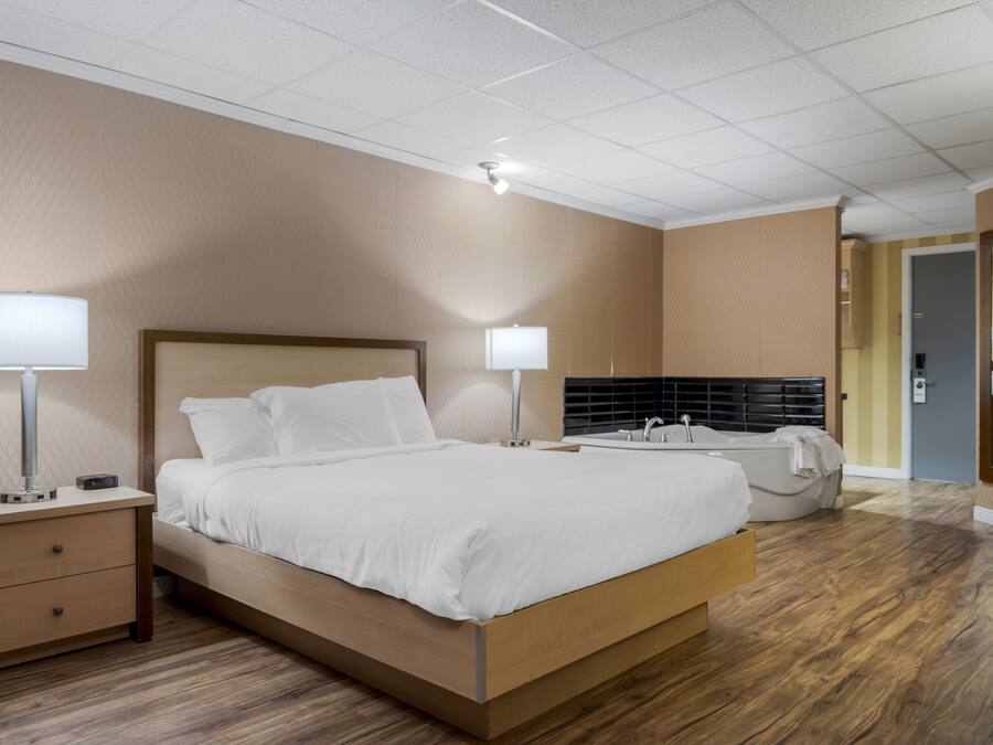 A modern hotel room with a wooden bed, bedside lamps, a bathroom with a bathtub, and a wooden floor.