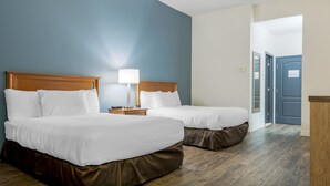 Et hotelværelse med to senge, trægavle, hvide sengetæpper, et sengebord med en lampe og en trægulv.