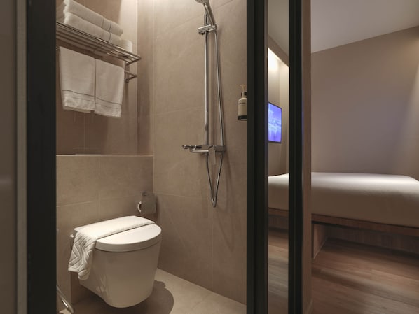 Un baño moderno con ducha, inodoro y una cama visible a través de un vidrio.