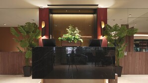 A reception desk with a marble top, two potted plants, and a wooden backdrop. - Hotel 1900 @ Chinatown (Singapore)