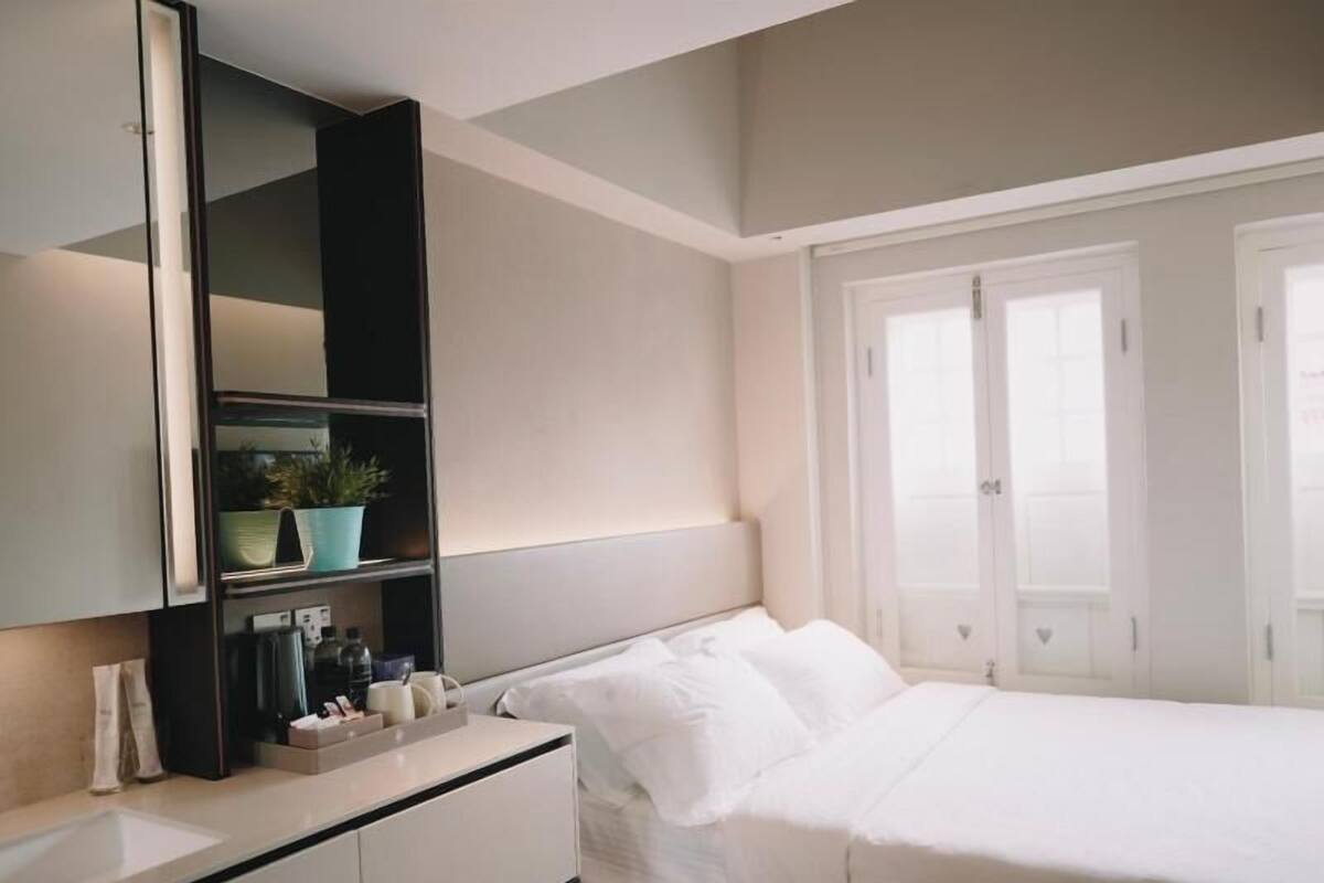 A bedroom with a bed, a bedside table, a mirror, and a shelf with a plant.