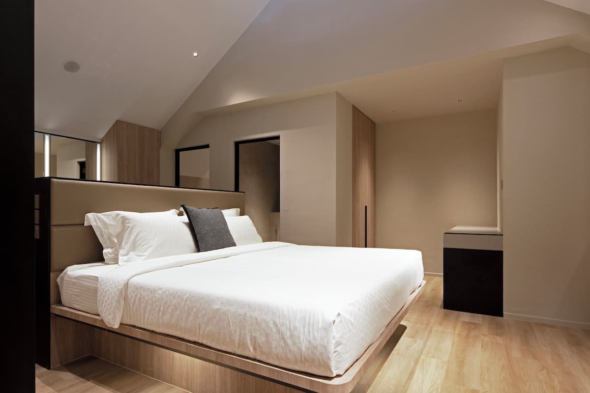 A modern bedroom with a bed, built-in headboard, and a small bedside table.