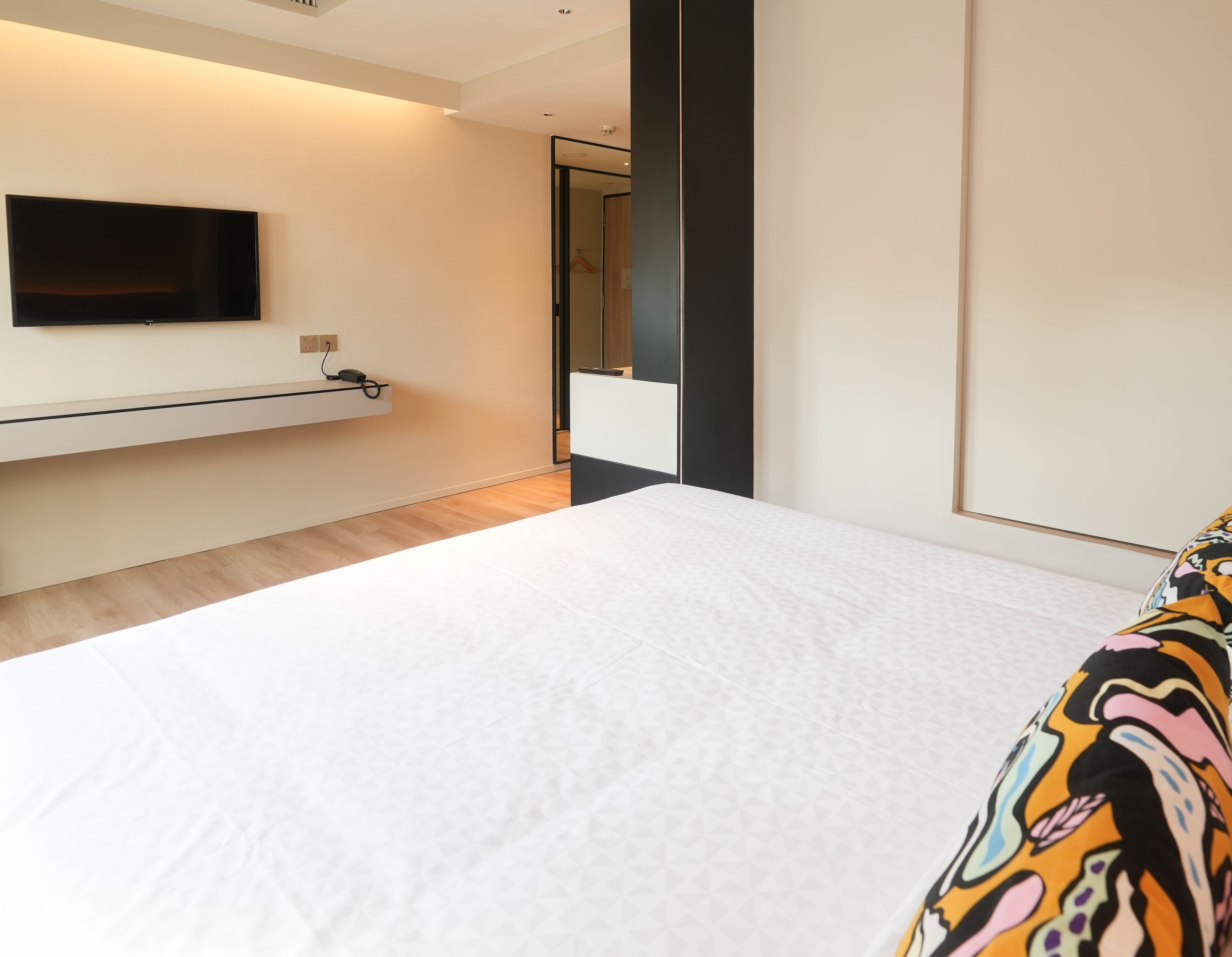 A modern hotel room with a large bed, a mounted TV, and a minimalist design.