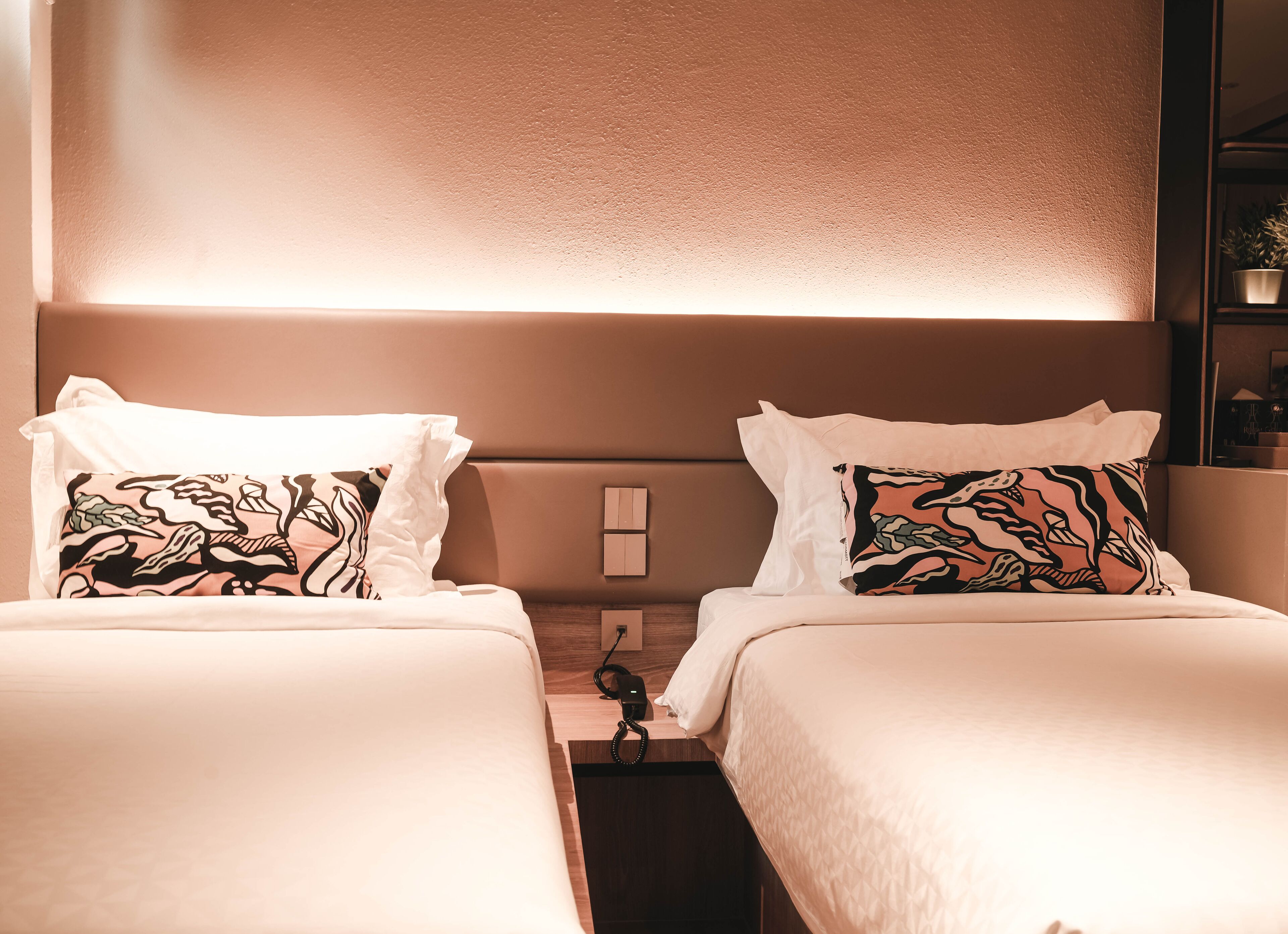 A hotel room with two beds, each with a patterned pillow and a white bedspread.