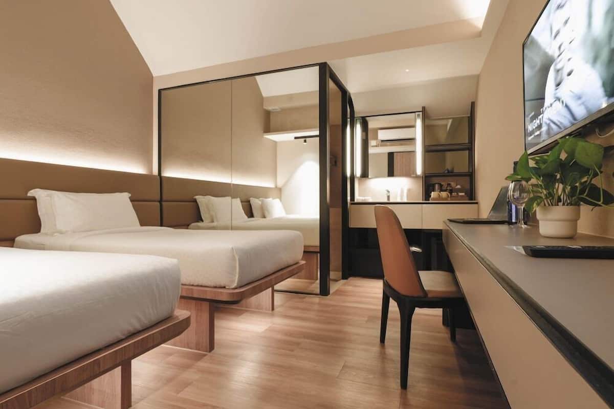 A modern hotel room with two beds, a desk, a chair, and a large mirror.