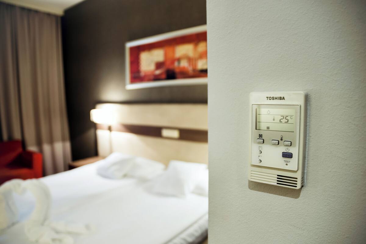 A hotel room with a bed, a wall-mounted thermostat, and a painting above the bed.