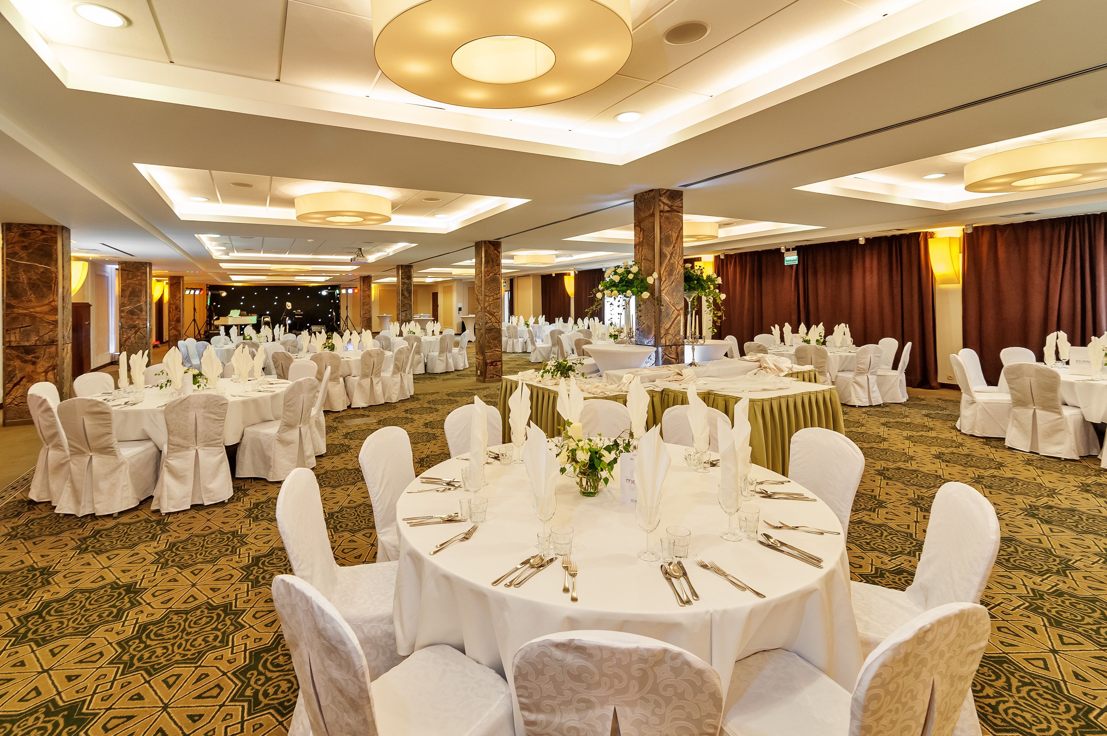A banquet hall with round tables set for a formal event, featuring white tablecloths, chairs, and floral centerpieces.