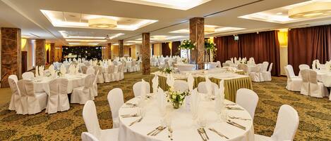A banquet hall with round tables set for a formal event, featuring white tablecloths, chairs, and floral centerpieces.