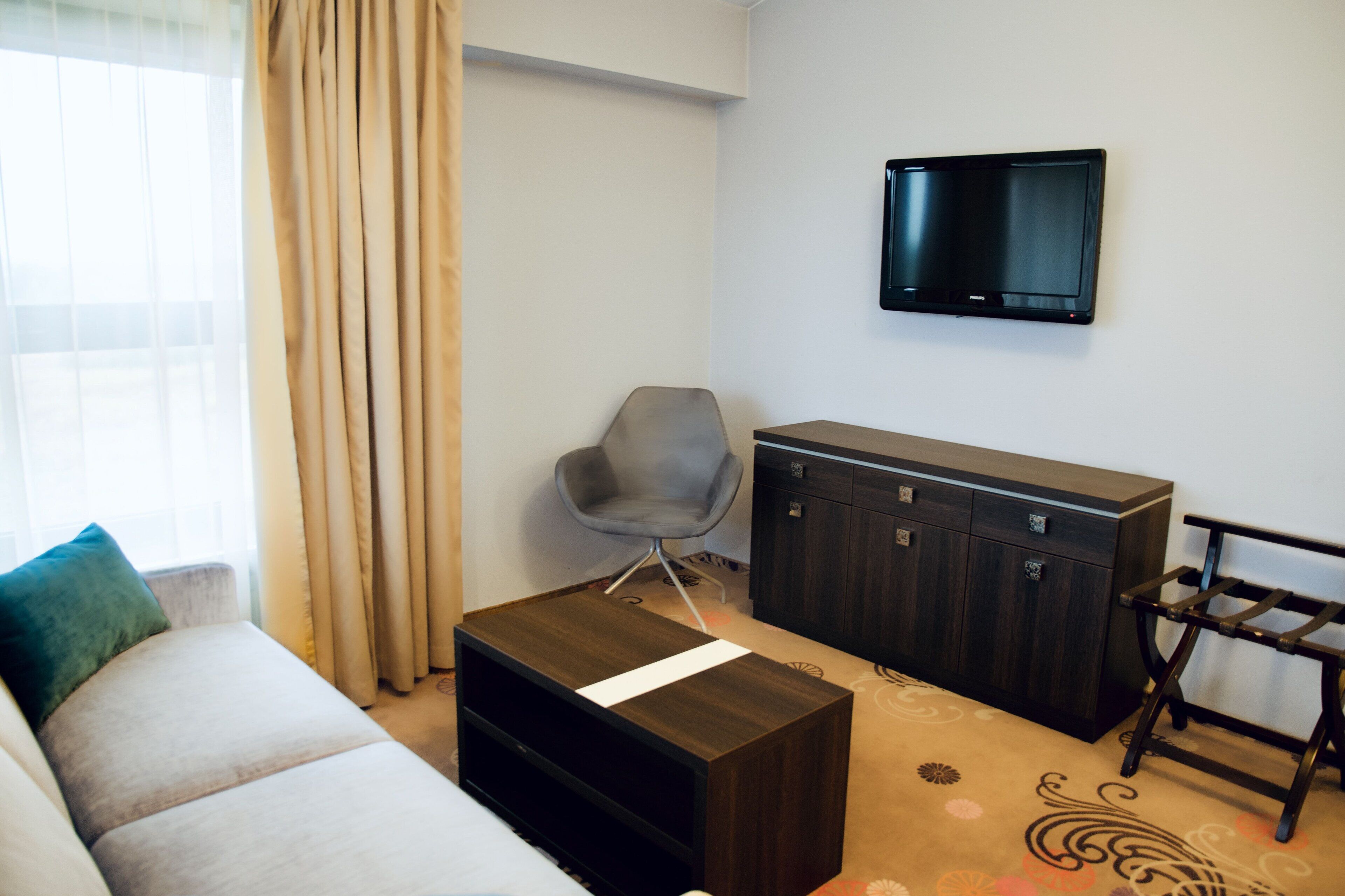 Una sala moderna con un sofá, una pequeña mesa de centro de madera, un sillón gris, un aparador de madera oscura y un televisor montado en la pared.
