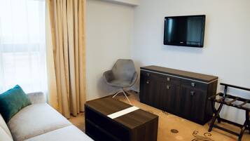 Una sala moderna con un sofá, una pequeña mesa de centro de madera, un sillón gris, un aparador de madera oscura y un televisor montado en la pared.