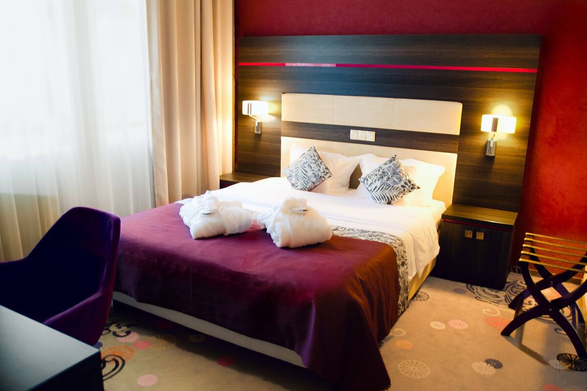 A hotel room with a bed, two bedside lamps, a chair, and a desk.