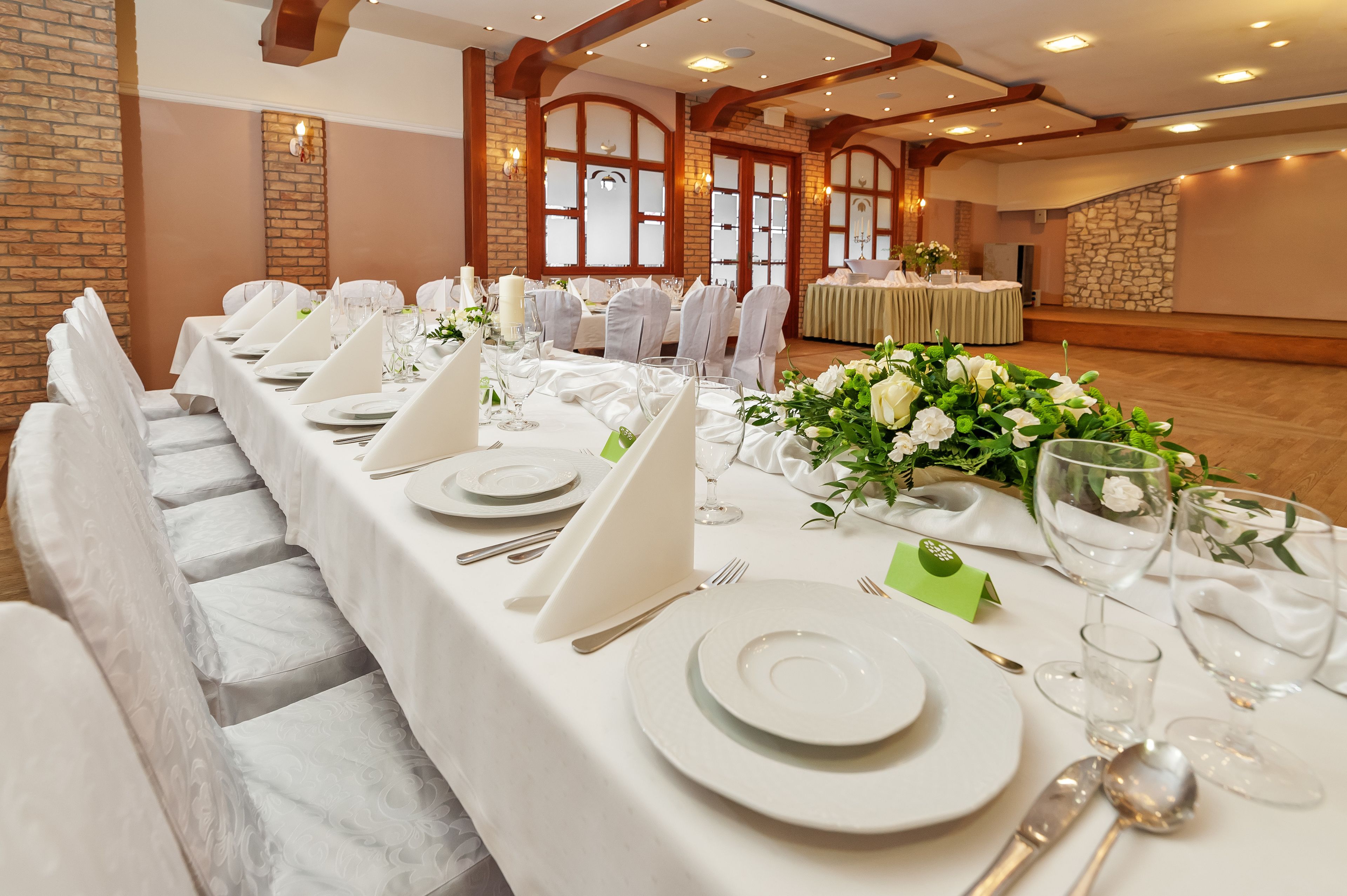Un gran saló de banquets amb llargues taules preparades per a un esdeveniment formal, amb estovalls blancs, plats i recipients de vidre.