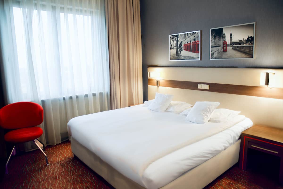 A hotel room with a large bed, a red chair, and two framed pictures on the wall.
