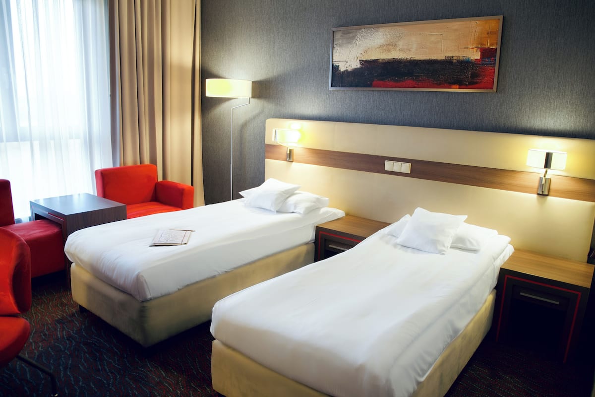 A hotel room with two beds, a desk, a chair, and a lamp.