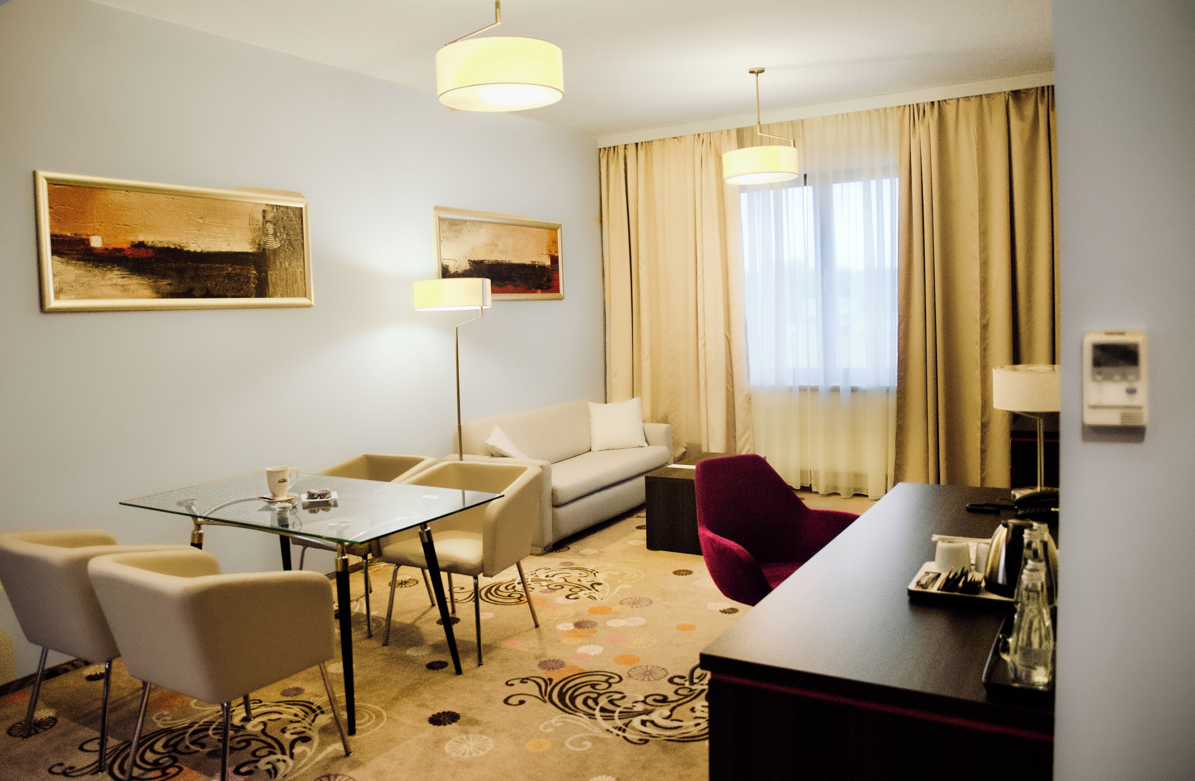 Una camera d'albergo con un tavolo da pranzo in vetro, una poltrona, una sedia rossa e due quadri alle pareti.