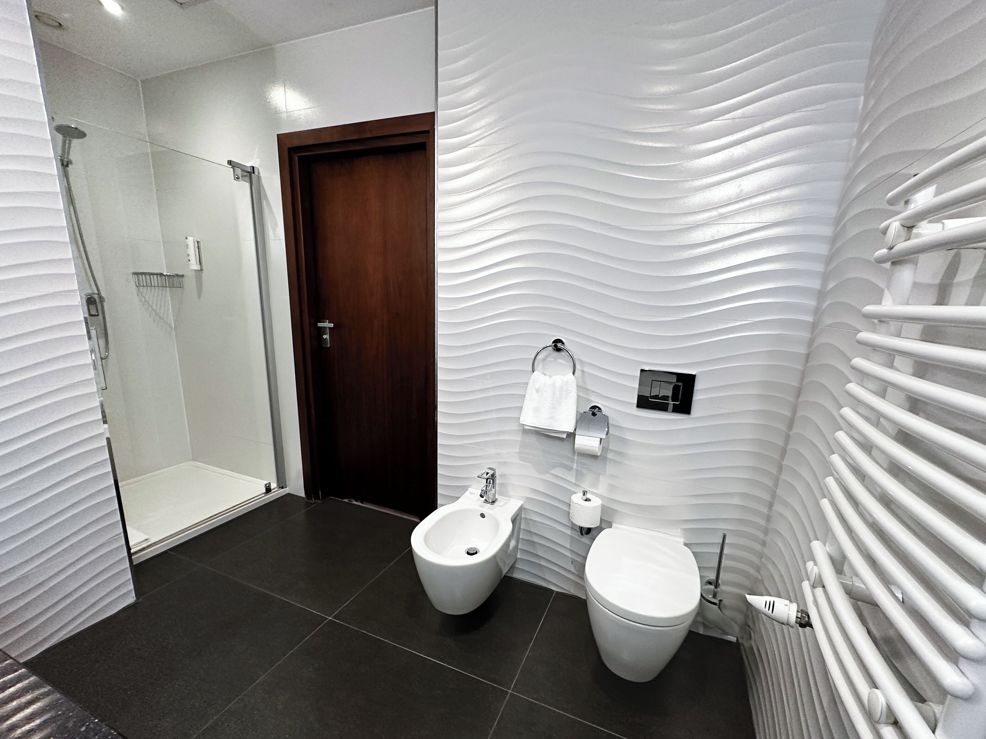 A modern bathroom with a shower, bidet, toilet, and a unique textured wall design.