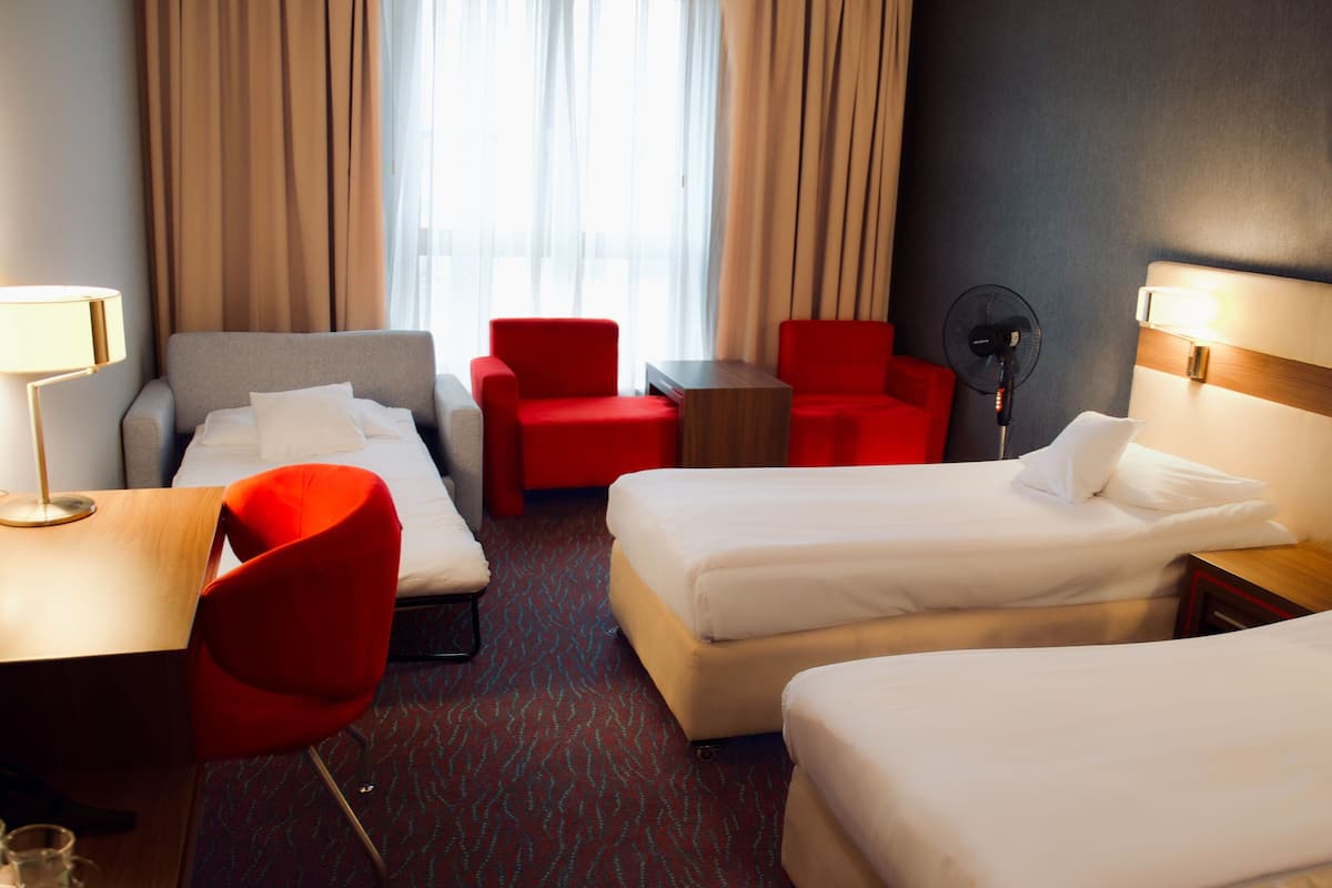 A hotel room with two beds, a desk, a chair, a table, and a fan.