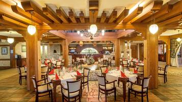 A restaurant with wooden beams and stone walls, tables set with red napkins and candles, and a bar area in the center.