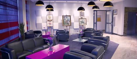 A lobby with leather sofas, a purple reception desk, and framed artwork on the walls.