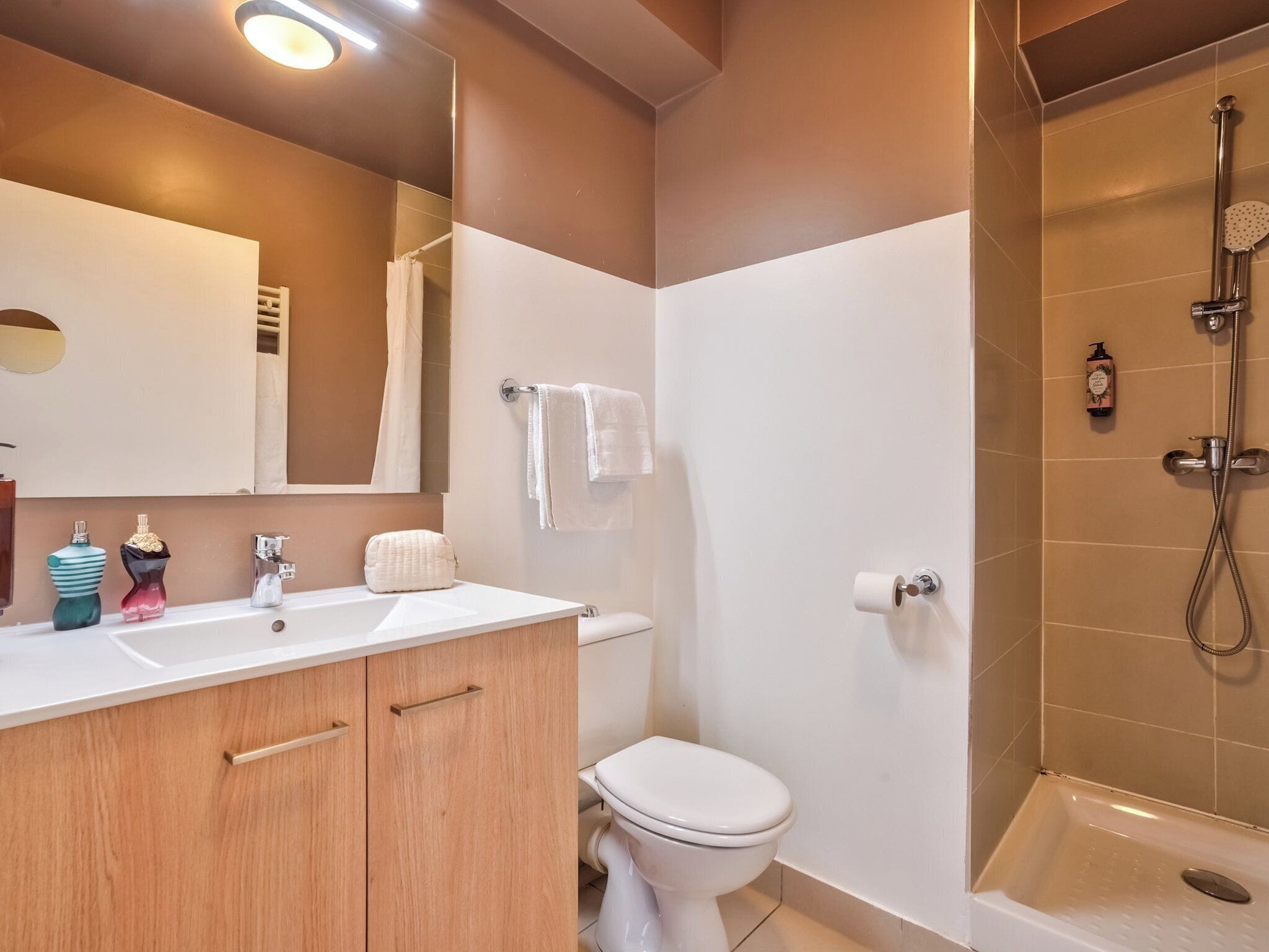 A bathroom with a white sink, wooden cabinets, a toilet, and a shower area.