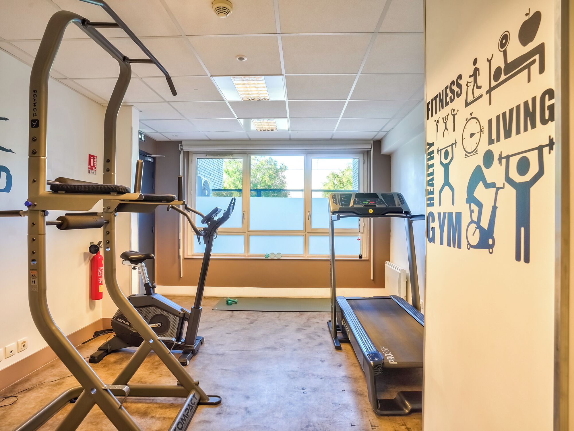 Una palestra con attrezzature per esercizi, un'ampia finestra e un muro motivazionale.