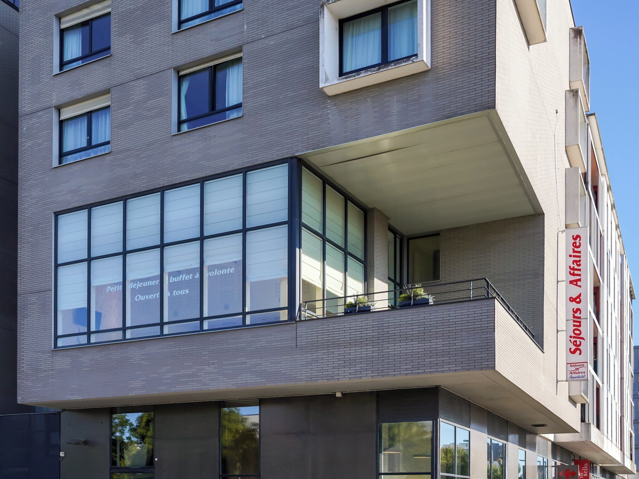 A modern building with large windows, a balcony with potted plants, and a sign reading "Séjours & Affaires."