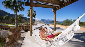 Un hamac sous une pergola en bois, avec vue sur les montagnes et les palmiers.