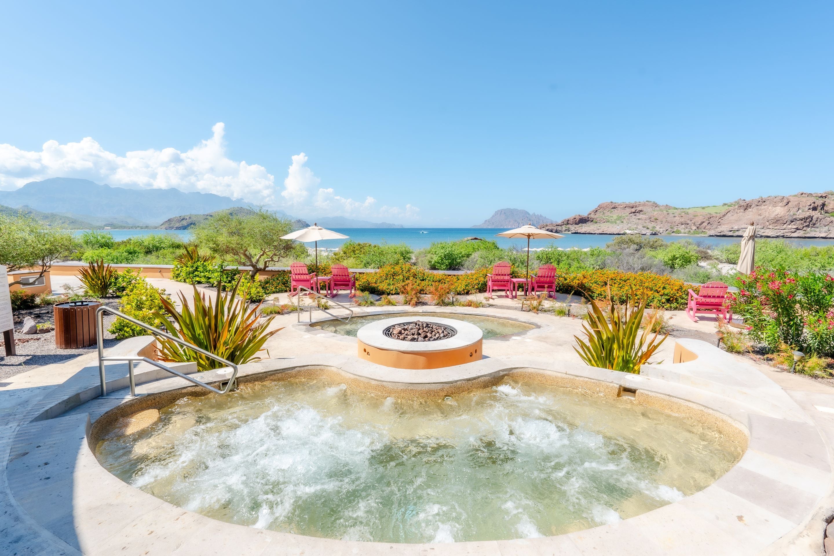 Un jacuzzi rodeado de sillas rojas y una piscina, con vistas al mar y montañas de fondo.