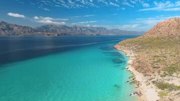 A coastal landscape with clear turquoise waters, a sandy beach, and rocky hills in the background.