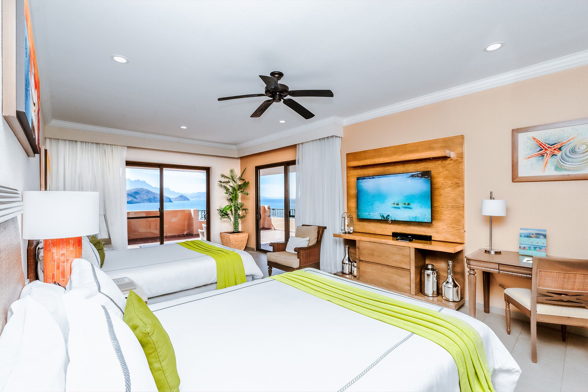 A hotel room with two beds, a television, a desk, and a balcony with a view.