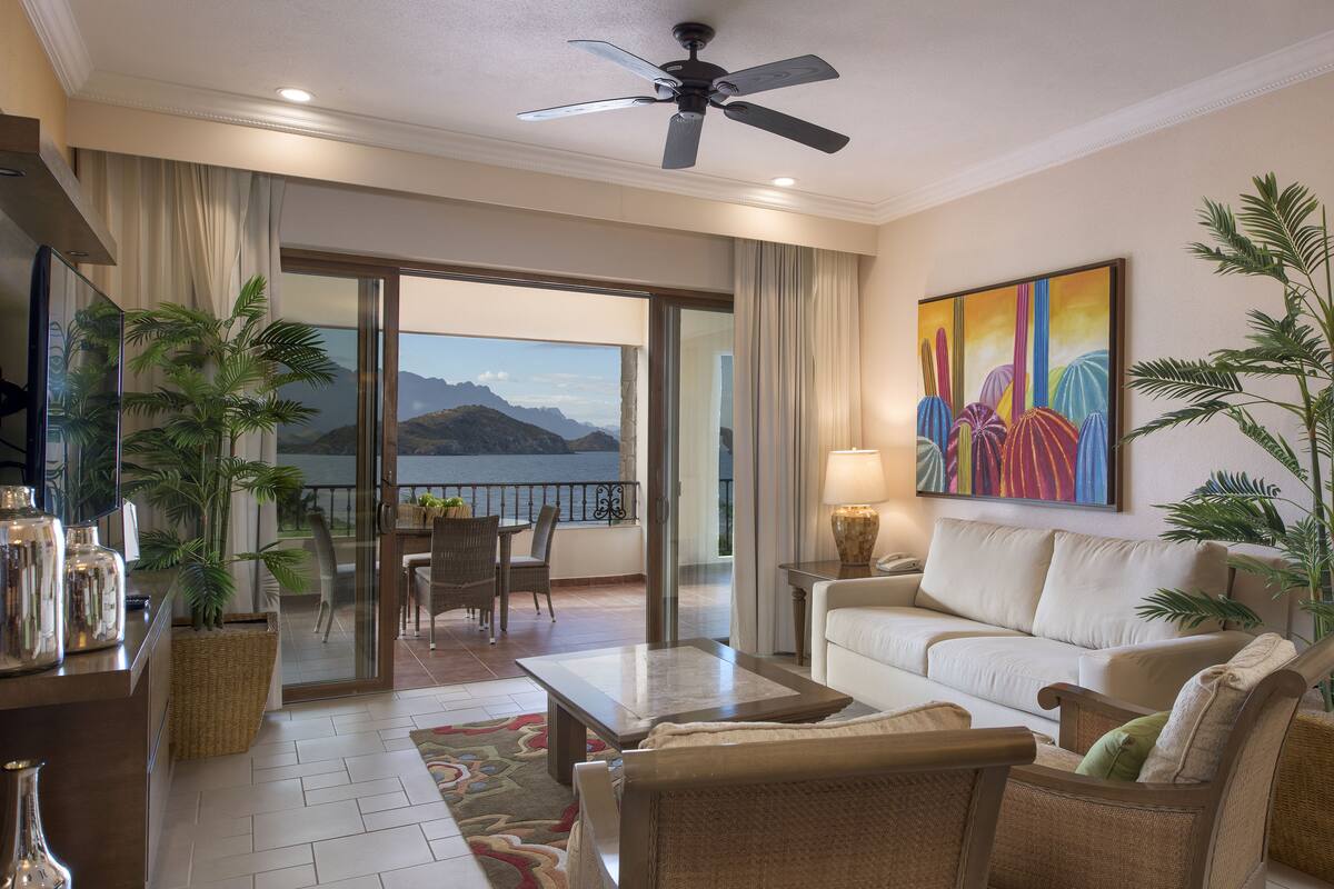 Ein Hotelzimmer mit Balkon, Deckenventilator, Sofa, Couchtisch und einem Gemälde.