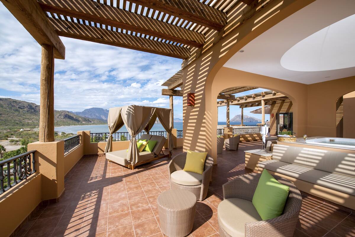 Eine Terrasse mit Korbmöbeln, Blick auf das Meer und eine gebirgige Landschaft.