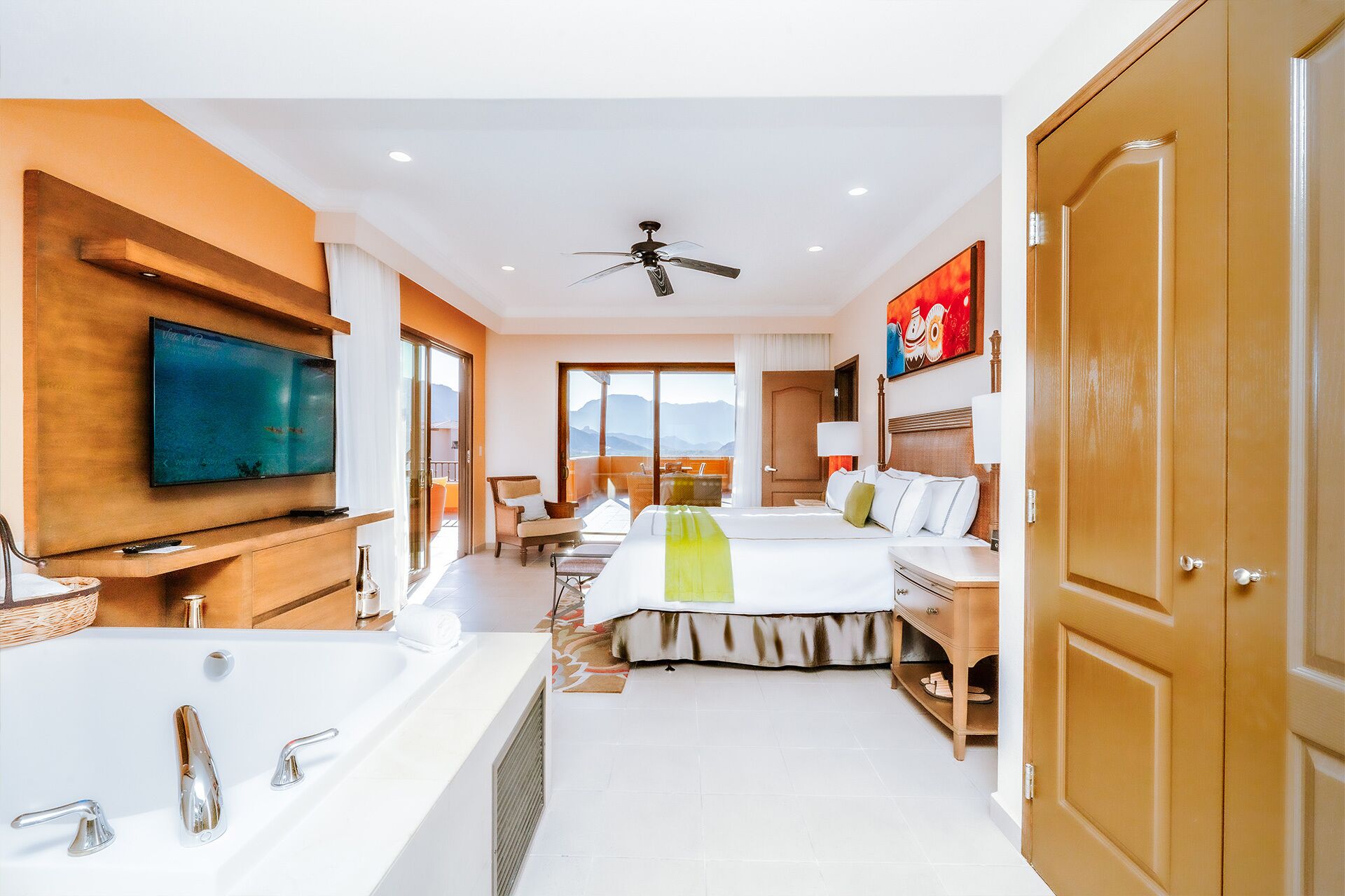 A hotel room with a large bed, a separate seating area, a television, a bathtub, and a door.