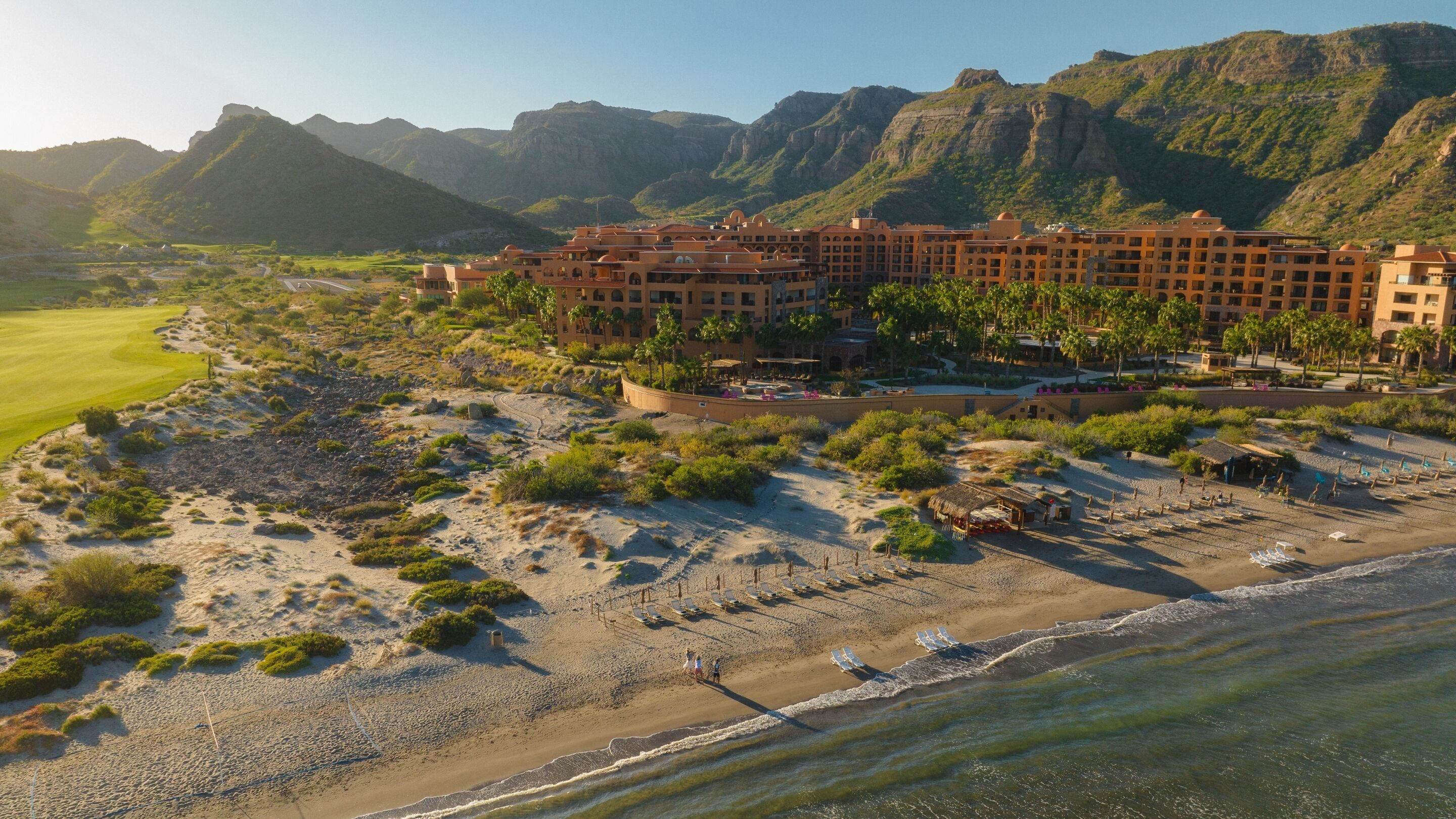 A resort with a beachfront, a golf course, and mountainous terrain in the background.