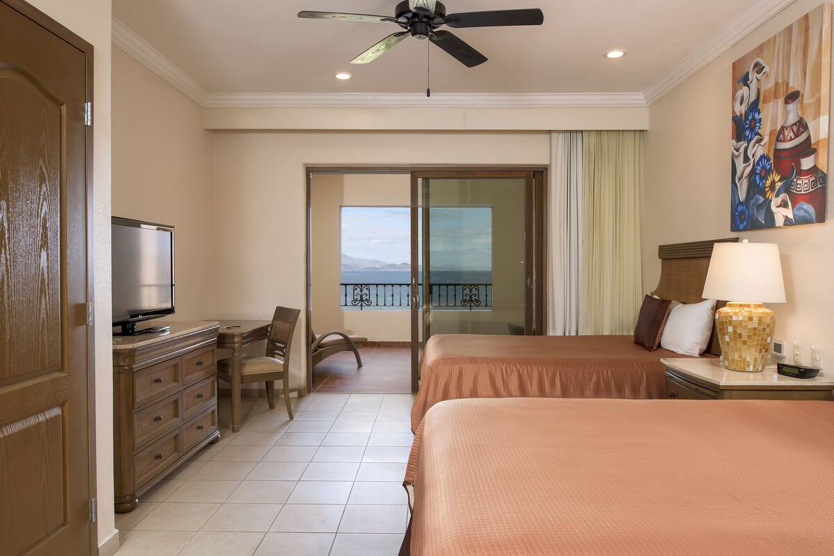 Ein Hotelzimmer mit Bett, Schreibtisch, Fernseher, Deckenventilator und einem Balkon mit Blick.