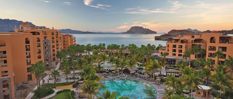 Un resort con una piscina central rodeada de palmeras y varios edificios con balcones con vista a la piscina.