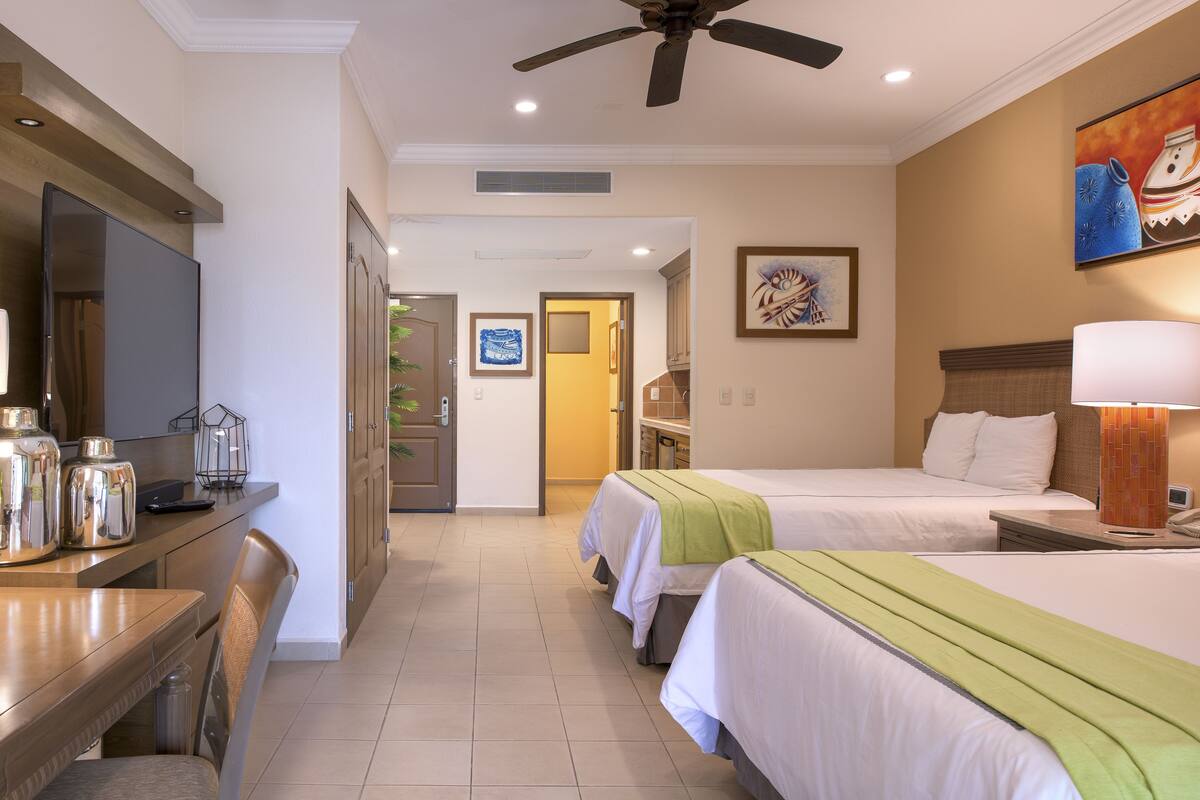 Ein Hotelzimmer mit zwei Betten, einem Schreibtisch mit Stuhl, einem Fernseher und einem Deckenventilator.